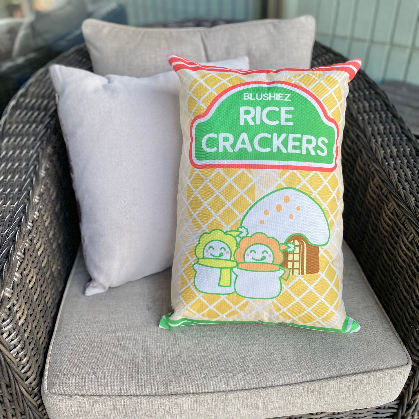 Pillow with a festive design resembling a snack-inspired pattern, placed on a gray chair. The pillow features a light orange background with orange and green stripes. It is accompanied by other solid color gray pillows, creating a coordinated arrangement.