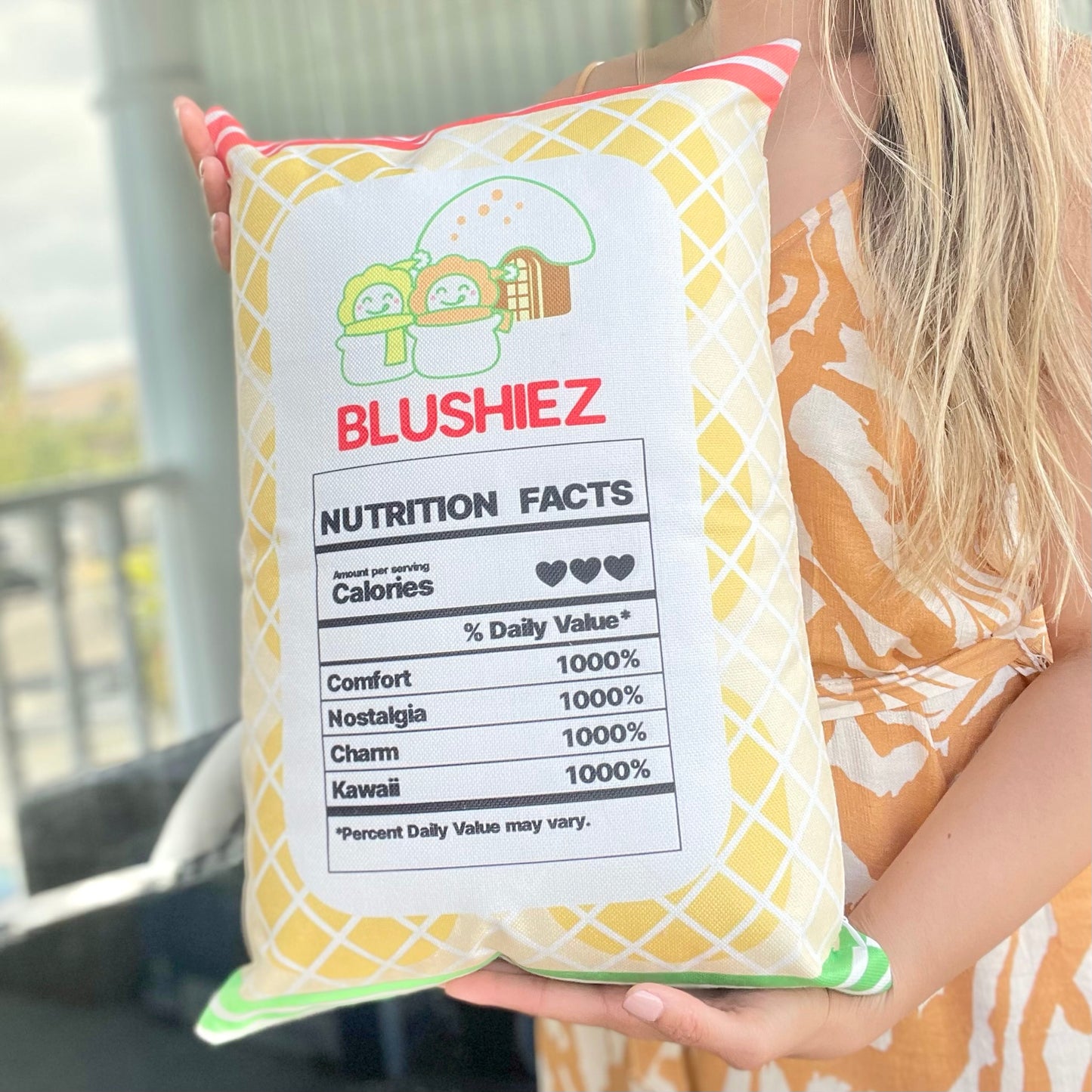 Back of the pillow with a festive design held in a woman's hands. The pillow features a light orange background with orange and green stripes, along with a playful nutrition facts label. The woman's hands provide a perspective of holding and displaying the back design of the pillow.