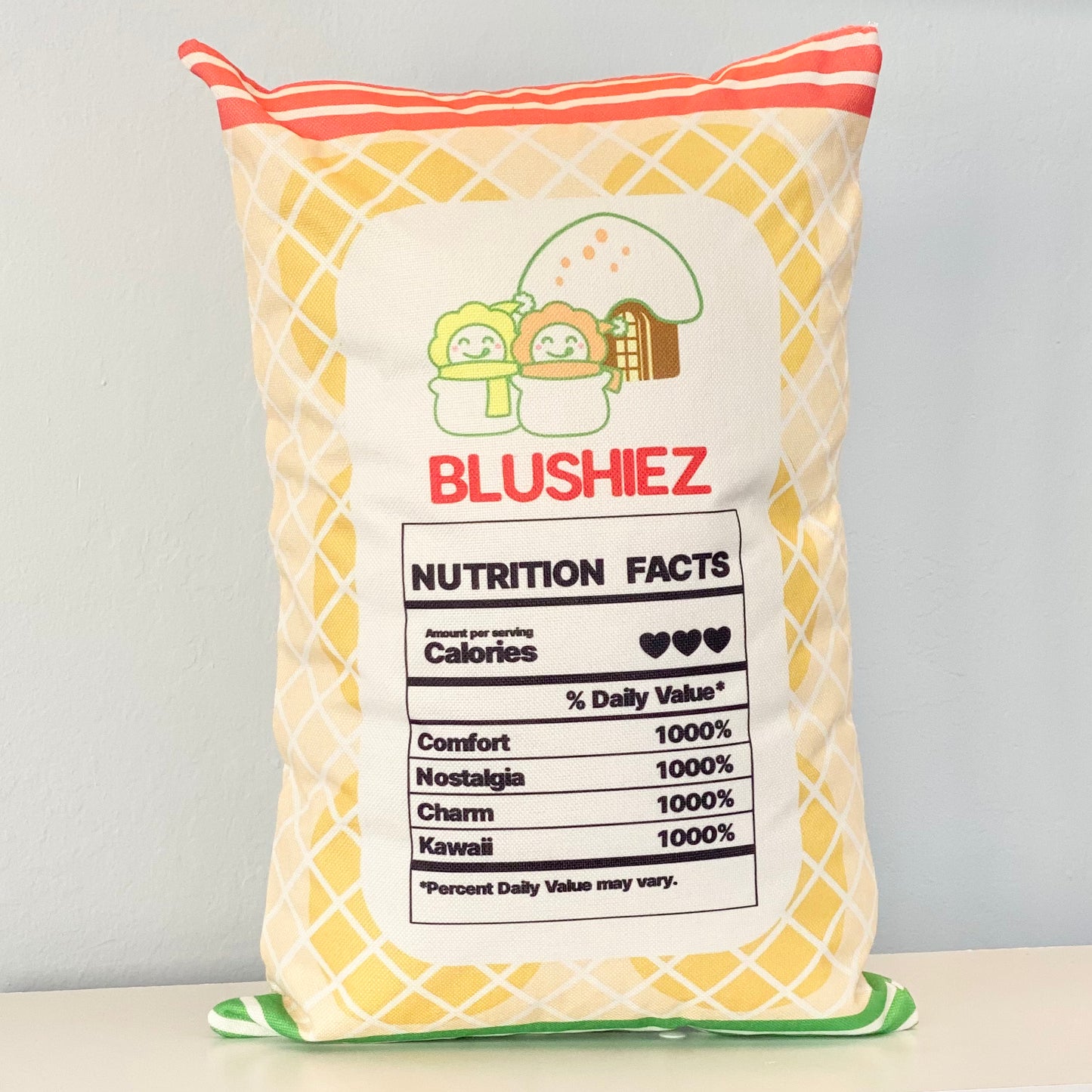 Back of the pillow with a festive snack-inspired design, held by a woman in her lap. The back side features a light orange background resembling rice crackers, with orange and green stripes. It includes a playful nutrition facts label with cute and whimsical information, adding a fun and imaginative touch to the design.