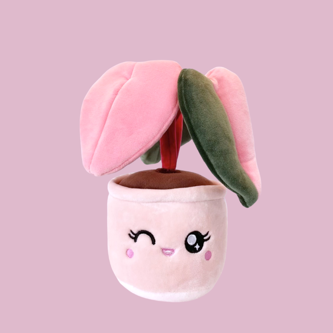 Plush toy of a potted plant with a pink pot and a winking face with eyelashes. The plant is a pink princess philodendron with three leaves. One leaf is green, another leaf is pink, and the third leaf has a split color pattern with the left side green and the right side pink. The stems of the plant are dark red.