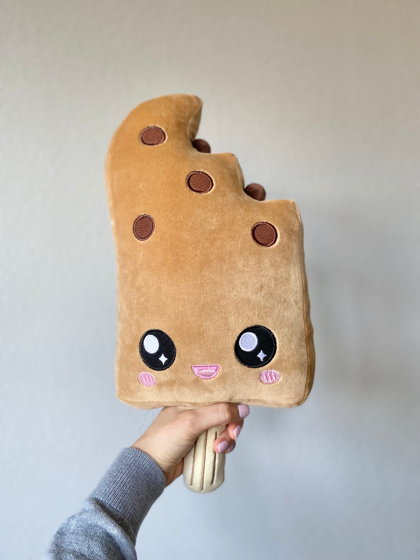 Plush toy of a boba ice cream bar with a smiling face, held by the bottom portion resembling a popsicle stick.