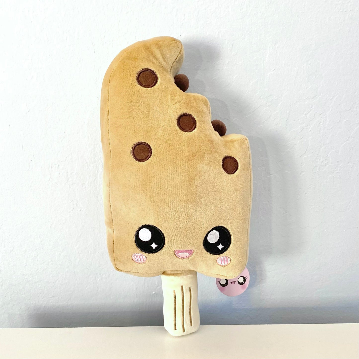 Plush toy of a boba ice cream bar with a cute open-mouth smiling face. The plush toy is shaped like an ice cream bar with a bite taken out of the top right corner.