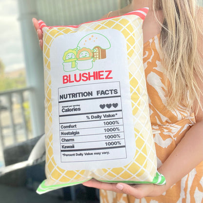 Back of the pillow with a festive design held in a woman's hands. The pillow features a light orange background with orange and green stripes, along with a playful nutrition facts label. The woman's hands provide a perspective of holding and displaying the back design of the pillow.